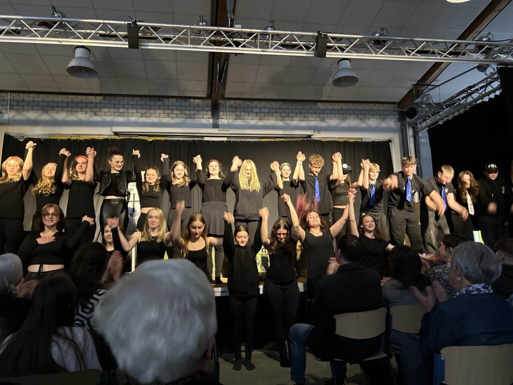 Schülerinnen und Schüler bei einer Theateraufführung, jubelnd und im Publikum applaudierend.