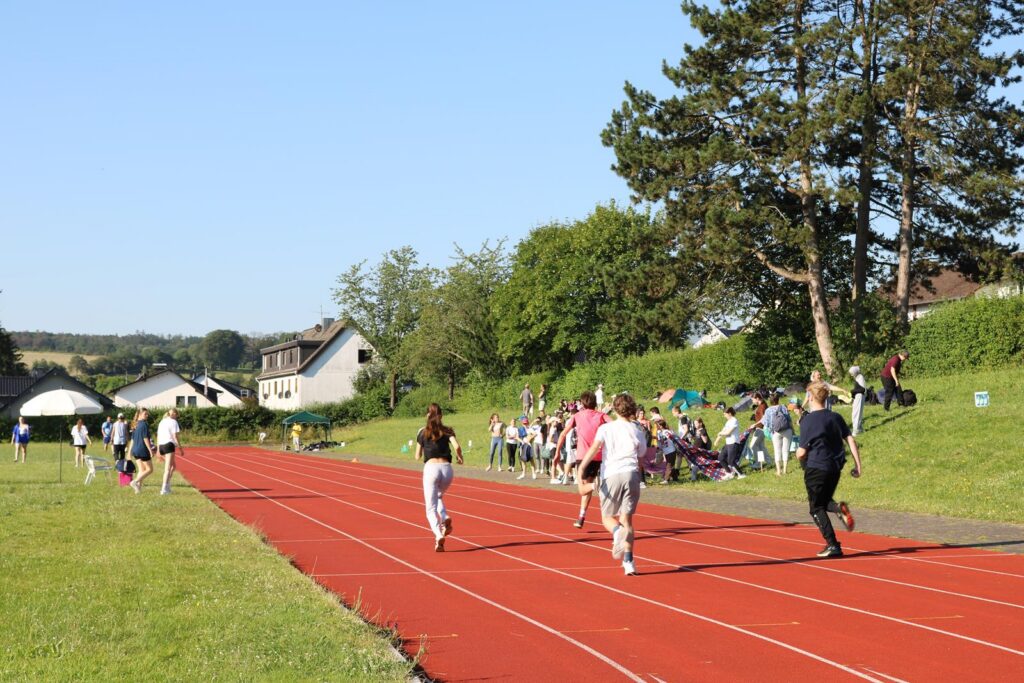 Schüler laufen auf einer roten Laufbahn, Zuschauer sitzen im Hintergrund.