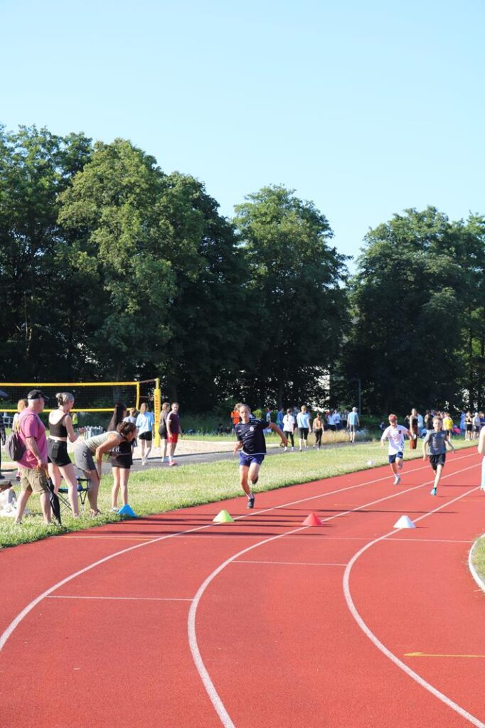 Läufer auf einer Sportbahn mit Zuschauern und Bäumen im Hintergrund.
