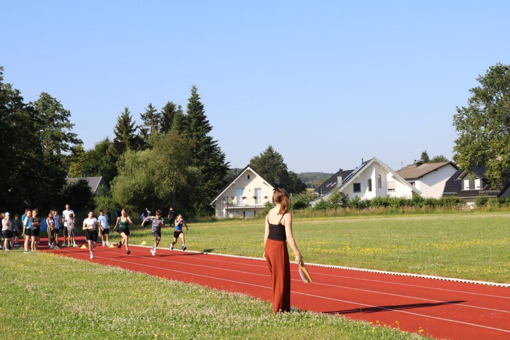 Läuferinnen und Läufer auf einer roten Rennbahn mit Zuschauerin im Vordergrund.