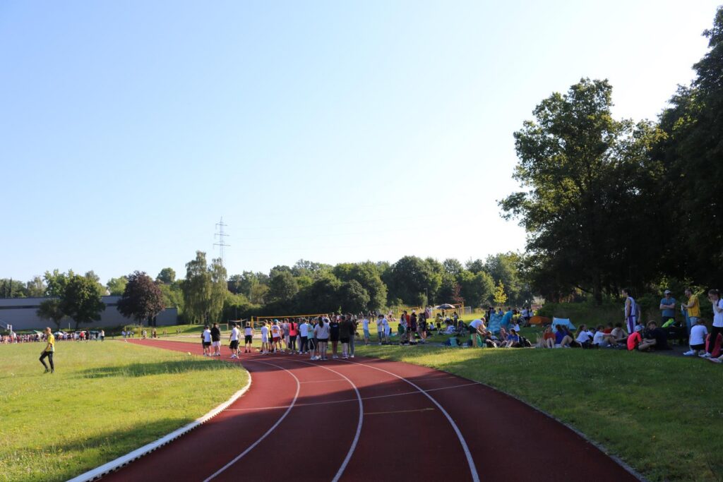 Laufbahn im Freien mit Zuschauern auf der Wiese im Hintergrund.