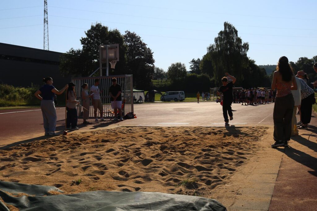 Schülerinnen und Schüler auf einem Sportplatz beim Basketball und Weitsprung.