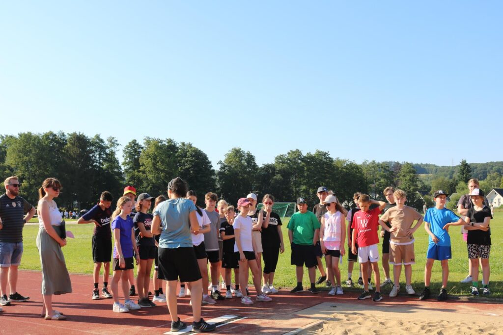Schülergruppen auf einem Sportplatz bei sonnigem Wetter.