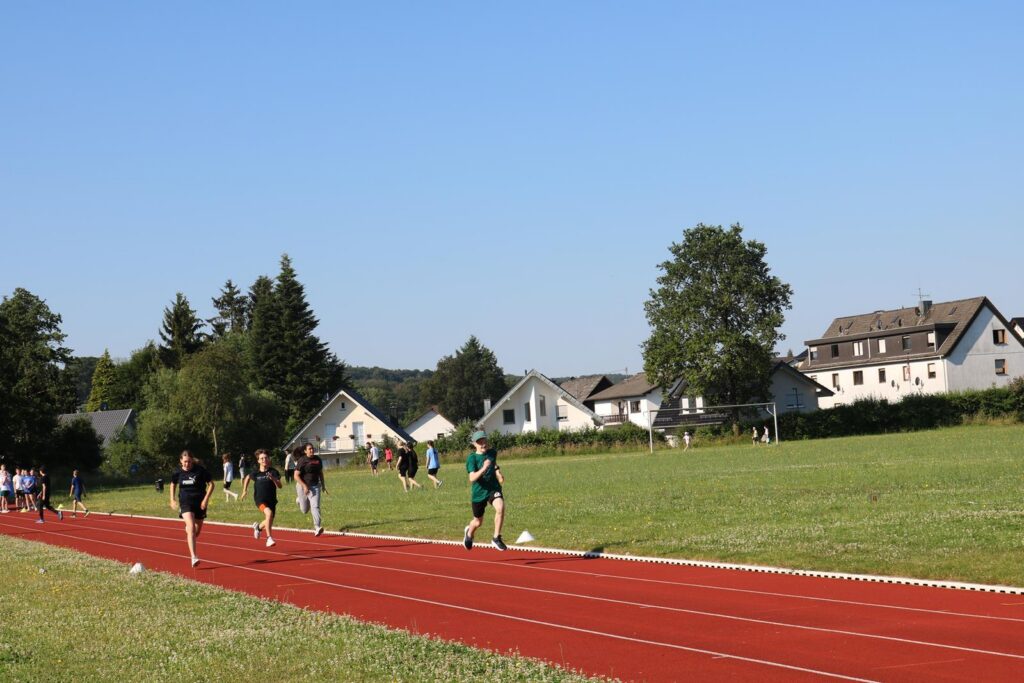 Läufer auf einer roten Laufbahn, Häuser im Hintergrund an einem sonnigen Tag.