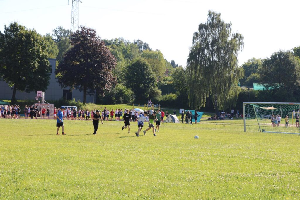Fußballspiel auf einem grünen Feld mit Zuschauern im Hintergrund.
