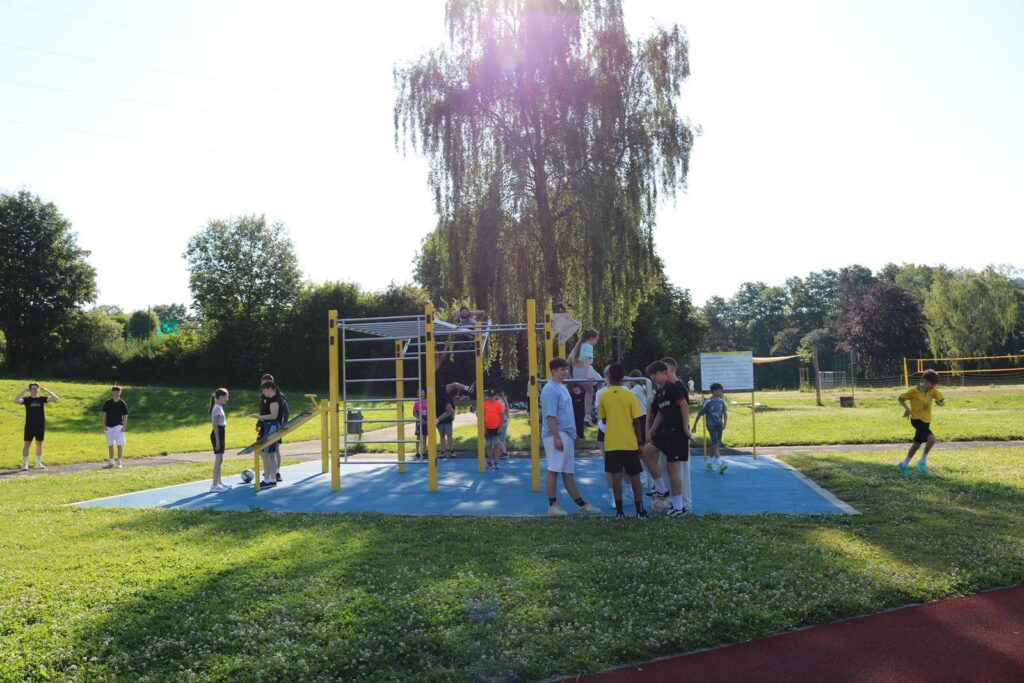 Kinder spielen auf einem Spielplatz mit Klettergerüst und Rasenfläche.