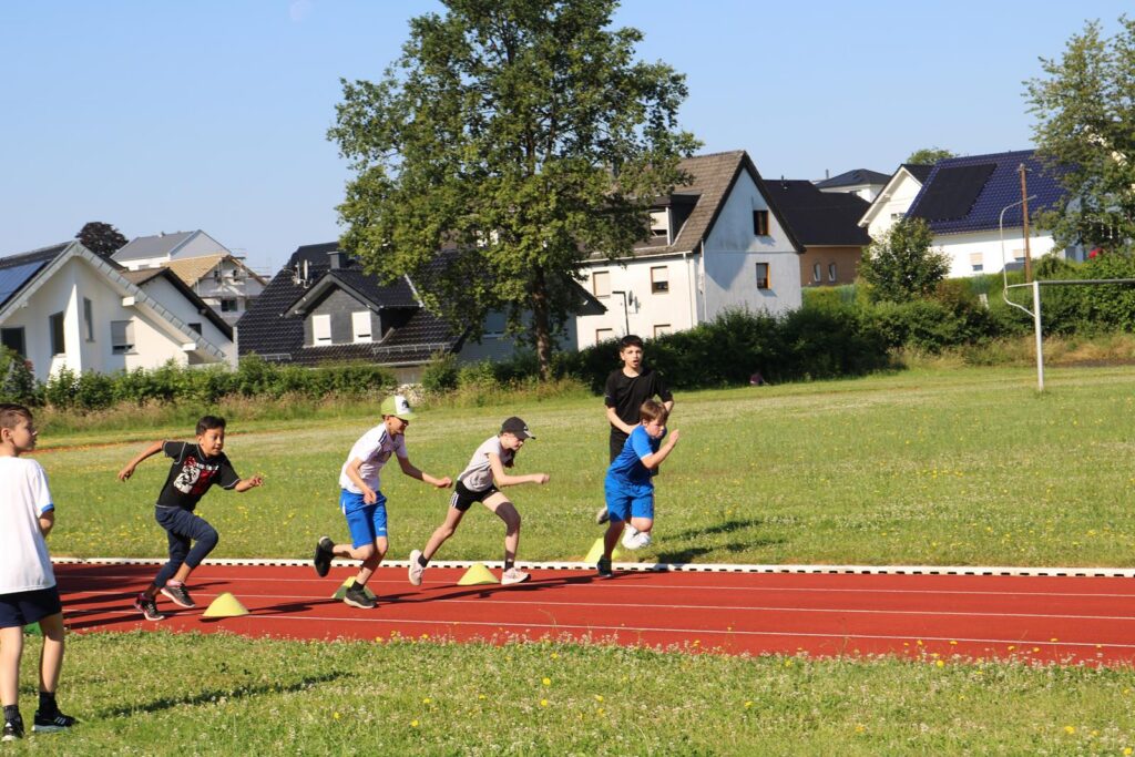 Kinder laufen auf einer Leichtathletikbahn, Trainier gibt Anweisungen.