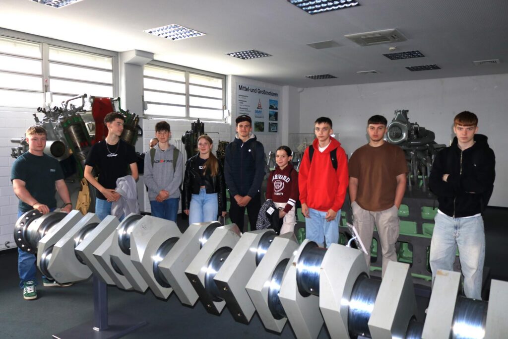 Gruppe von Schülern vor einem großen Motorenkomponenten-Modell in einem Ausstellungsraum.