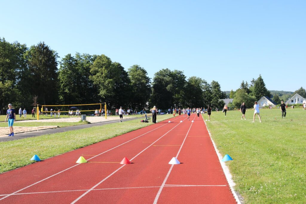 Sportveranstaltung auf einem Außensportplatz mit Laufbahn und Volleyballfeld.