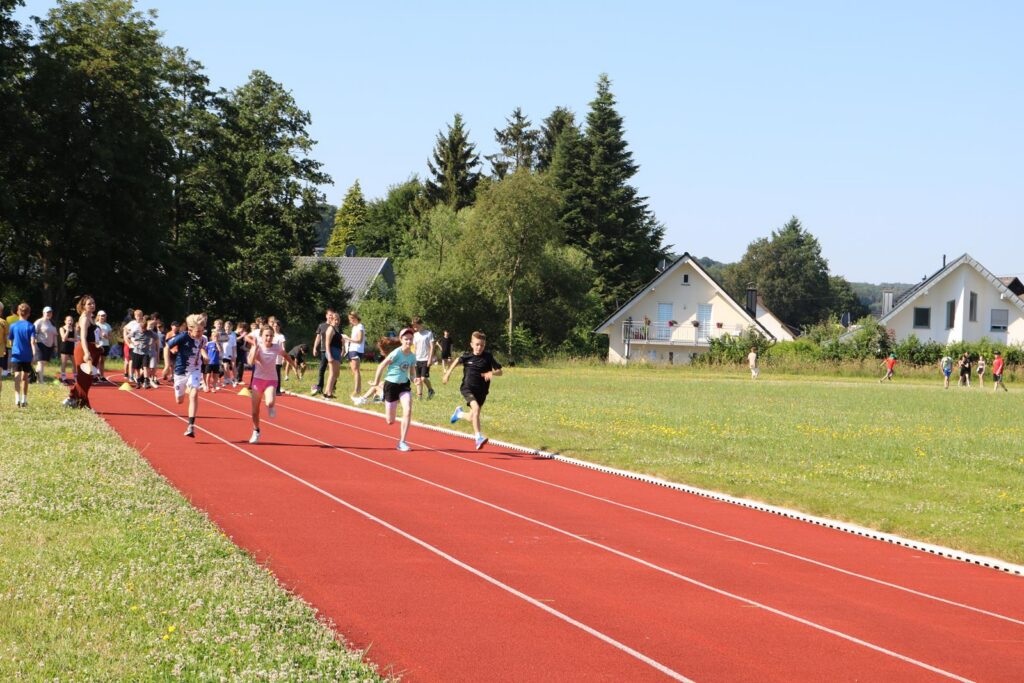 Schüler laufen auf einer roten Laufbahn bei sonnigem Wetter.