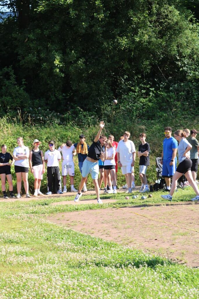 Schülerinnen und Schüler stehen in einer Reihe auf einem Sportplatz.