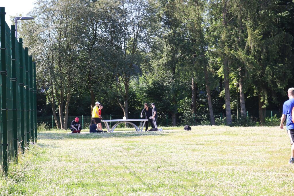 Spielende Schüler auf einem Sportplatz mit Bäumen im Hintergrund.