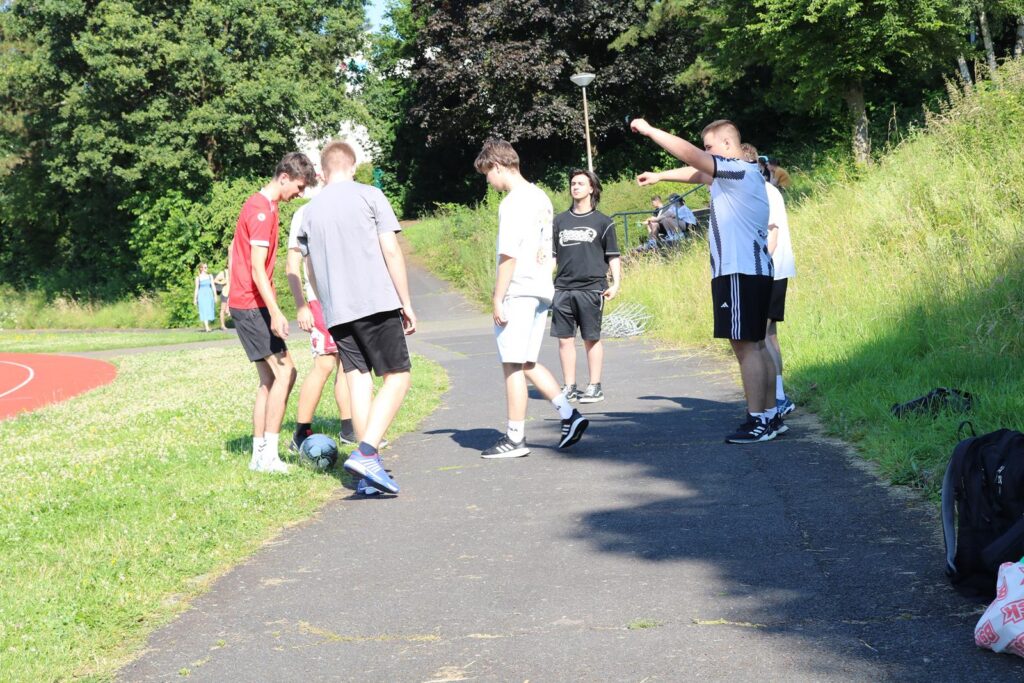 Fünf Jugendliche auf einem Weg, spielen Fußball und unterhalten sich.
