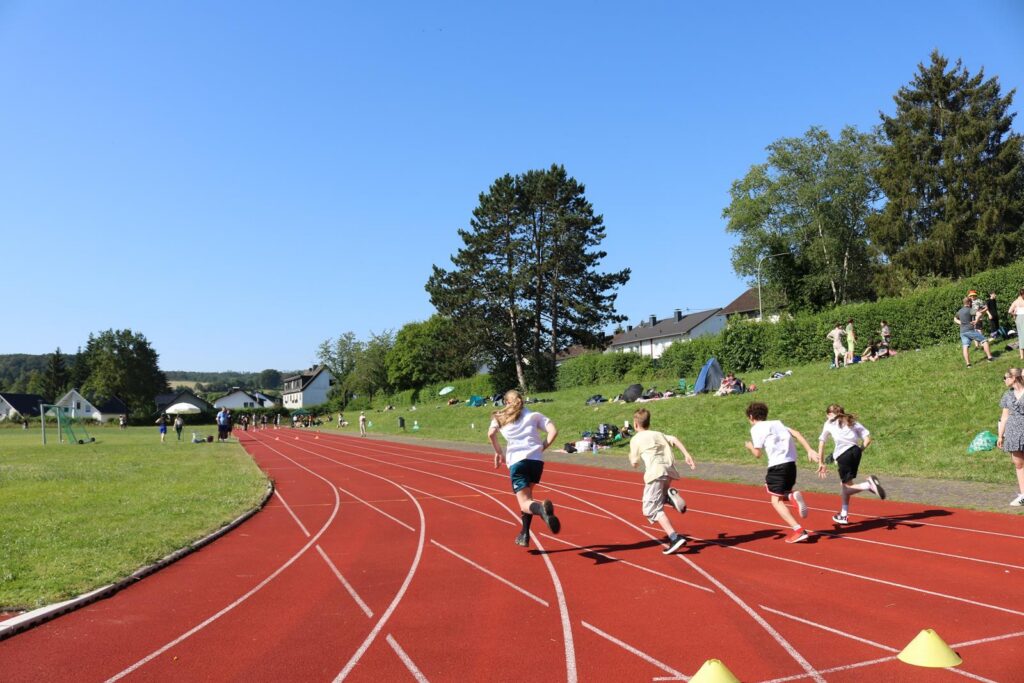 Schülerinnen und Schüler laufen auf einer roten Laufbahn bei sonnigem Wetter.