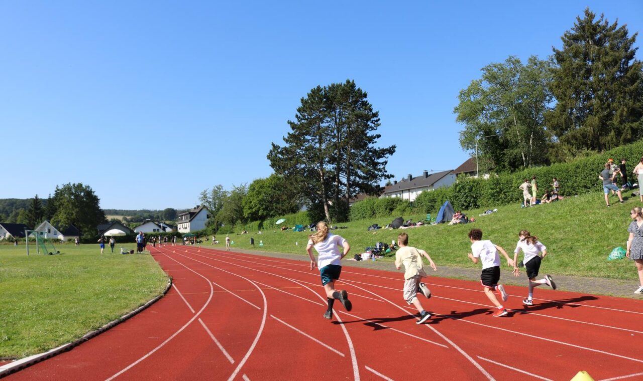 Schülerinnen und Schüler laufen auf einer roten Laufbahn bei sonnigem Wetter.