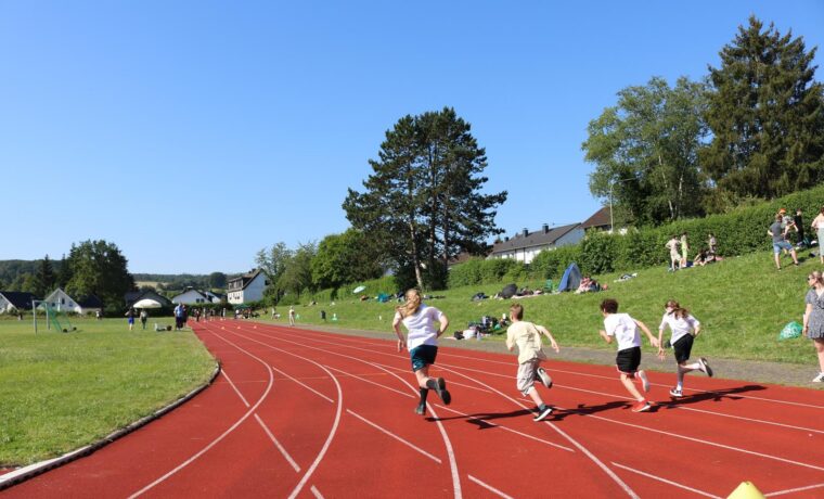 Schülerinnen und Schüler laufen auf einer roten Laufbahn bei sonnigem Wetter.