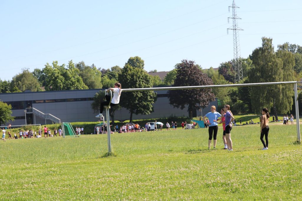 Ein Junge klettert auf das Tor, während drei Mädchen am Fußballfeld stehen.