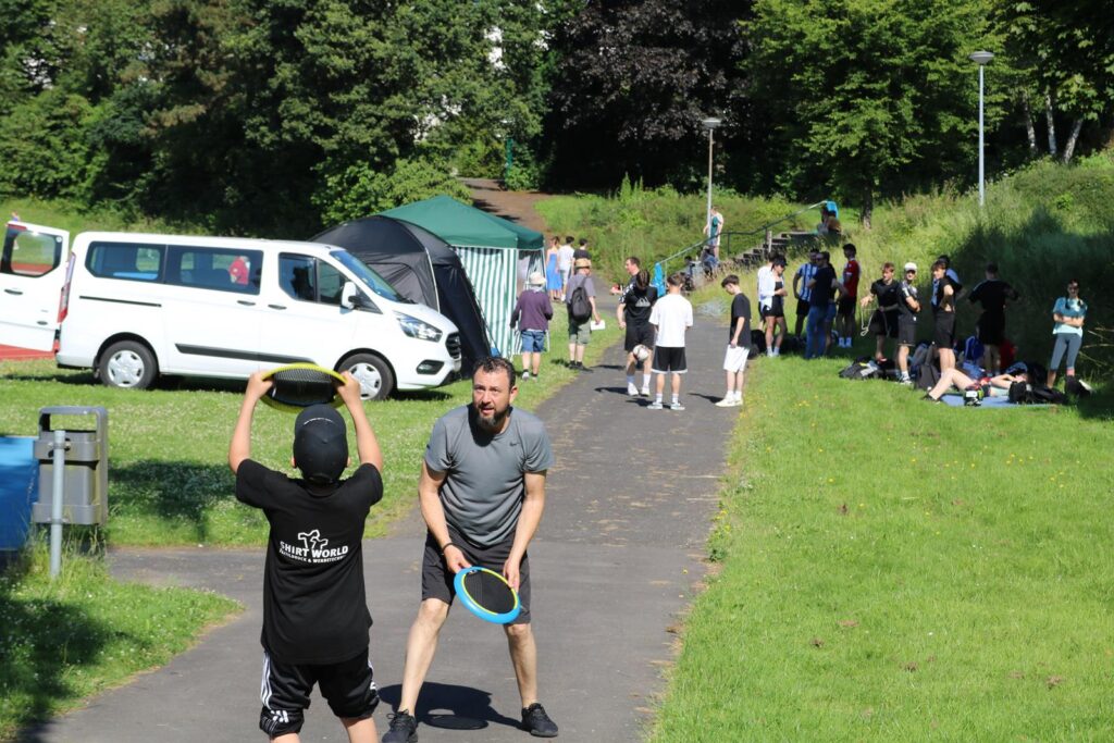 Menschen spielen Frisbee auf einem grünen Feld, im Hintergrund Autos und Zelte.