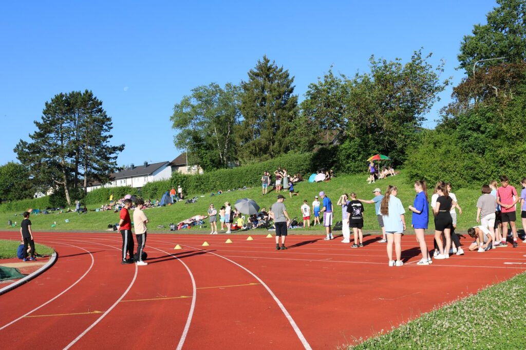 Sportveranstaltung auf einer Laufbahn mit Teilnehmern und Zuschauern im Hintergrund.