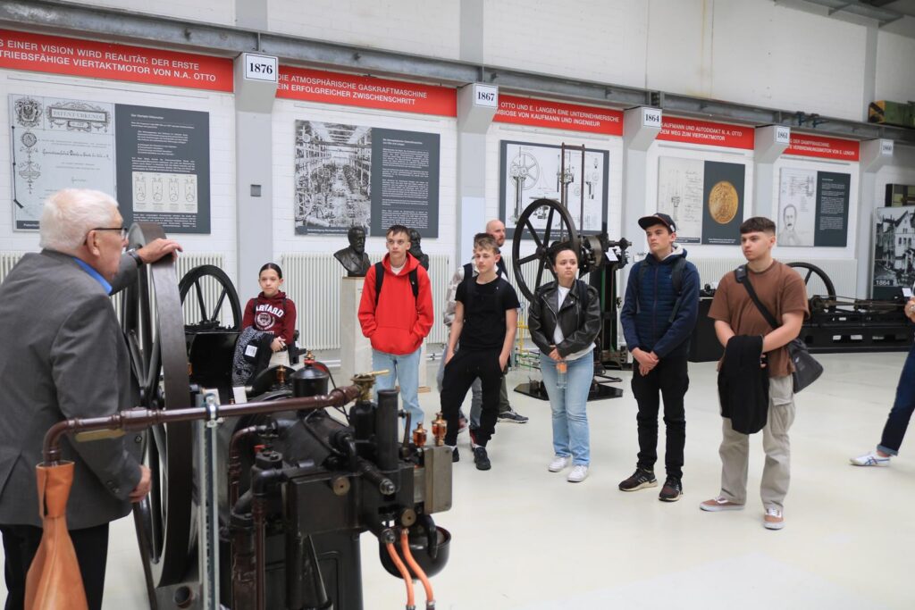 Schülergruppe hört einem Vortrag über Maschinen in einer Ausstellung zu.