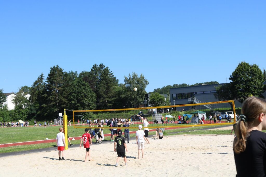Strandvolleyballfeld mit Kindern und Jugendlichen im Hintergrund, bei schönem Wetter.