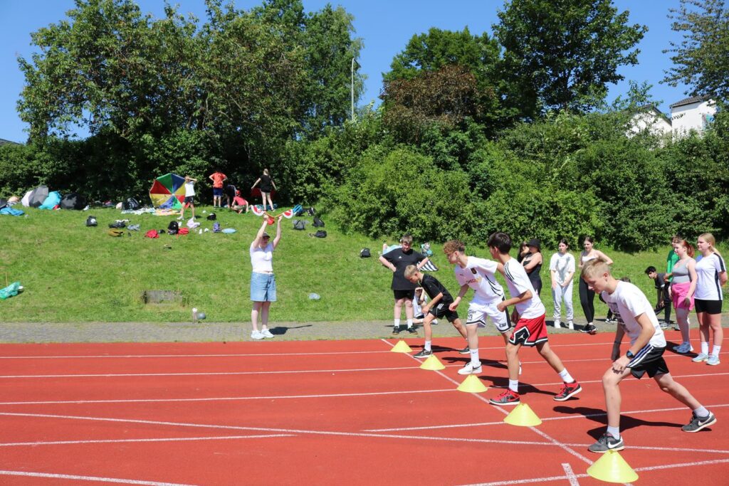 Athleten starten an der Startlinie auf einem Sportplatz. Zuschauer im Hintergrund.
