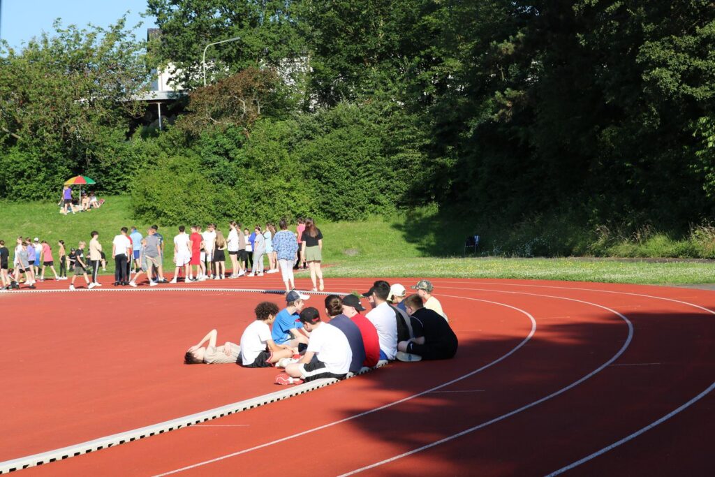 Sportveranstaltung auf einer Laufbahn mit Schülern und Zuschauern im Hintergrund.