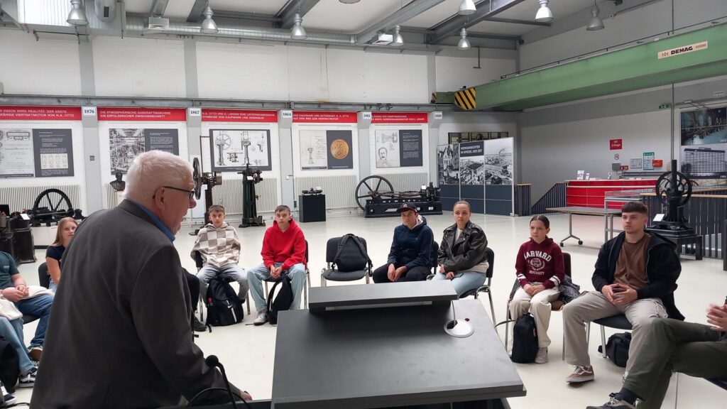 Ein Referent spricht vor einer Gruppe von Zuhörern in einem Ausstellungsraum.