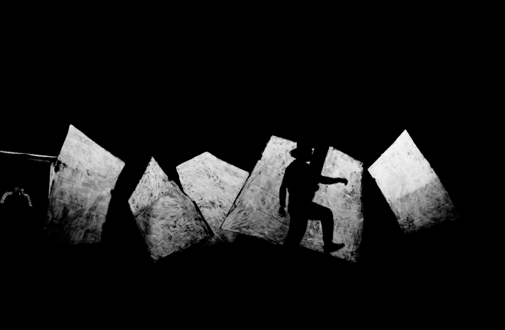 Silhouette einer Person, die auf schrägen, hellen Flächen in dunkler Umgebung steht.