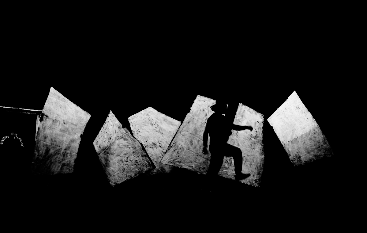 Silhouette einer Person, die auf schrägen, hellen Flächen in dunkler Umgebung steht.