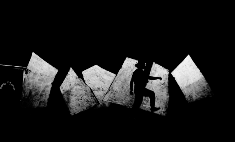 Silhouette einer Person, die auf schrägen, hellen Flächen in dunkler Umgebung steht.