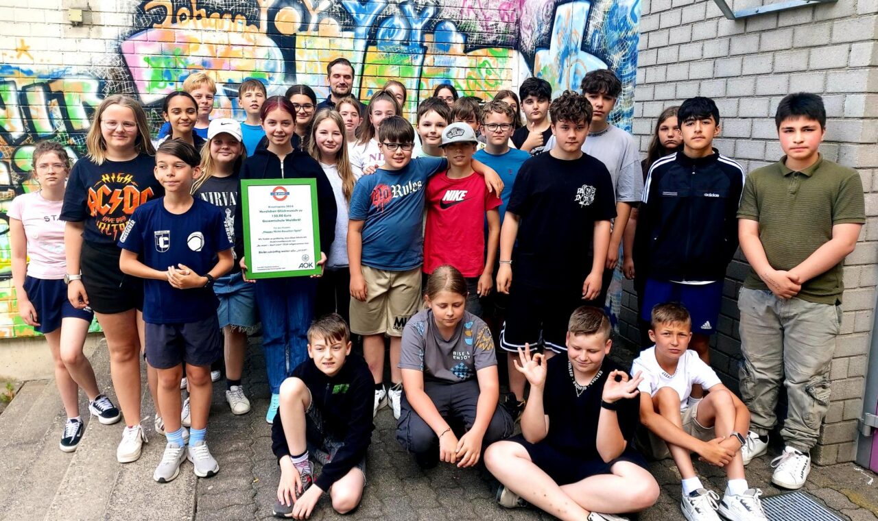 Gruppe von Schülern lächelt vor einer bunten Graffiti-Wand.