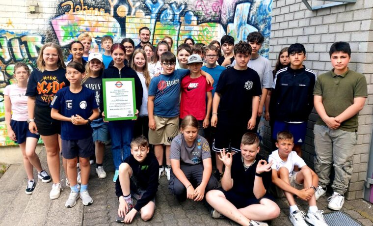 Gruppe von Schülern lächelt vor einer bunten Graffiti-Wand.