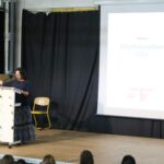 Eine Person steht an einem Rednerpult vor einer Präsentation.