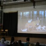 Eine Person spricht vor einer Präsentation mit Tieren im Wald.