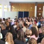 Publikum in einem großen Raum bei einer Veranstaltung, viele Menschen mit bunten Ballons.