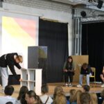 Schüler führen eine Präsentation auf der Bühne vor Publikum durch.