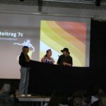 Schauspieler präsentieren einen Beitrag auf einer Bühne vor Publikum.