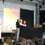 Schüler führen ein Theaterstück auf der Bühne vor Publikum auf.