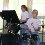 Zwei Kinder spielen in einem Musikraum Schlagzeug.