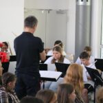 Schülerblasmusikgruppe spielt, ein Lehrer steht vorne und dirigiert.