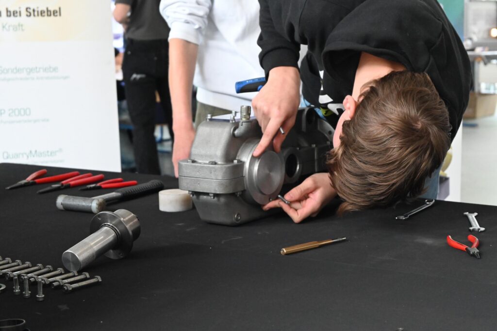 Ein Schüler arbeitet an einem Motorbauteil am Tisch mit Werkzeugen.