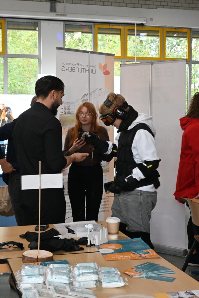 Messebesucher in VR-Ausrüstung sprechen mit einer Person am Stand.