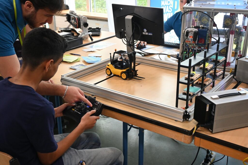 Schüler steuert mithilfe eines Controllers ein ferngesteuertes Fahrzeug in einem Technikraum.