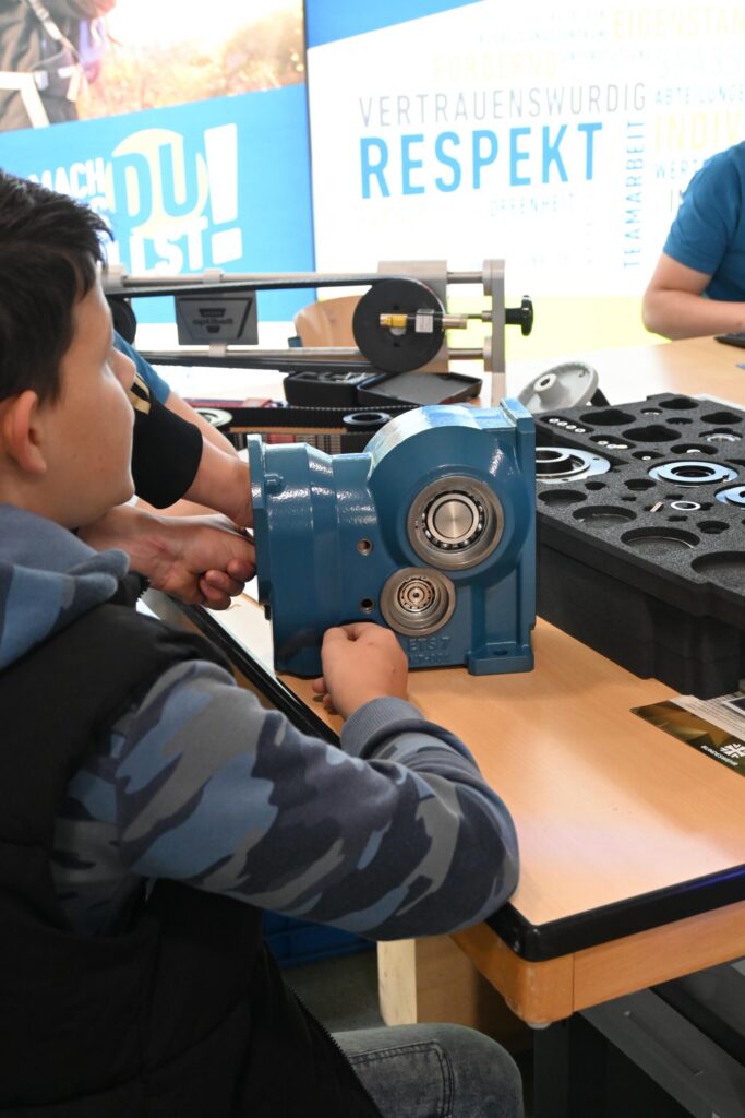 Schüler arbeitet an einer blauen Maschinenkomponente am Tisch.