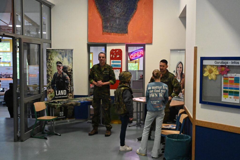 Informationsstand mit Bundeswehrmitarbeitern und interessierten Schülern in einer Schulumgebung.