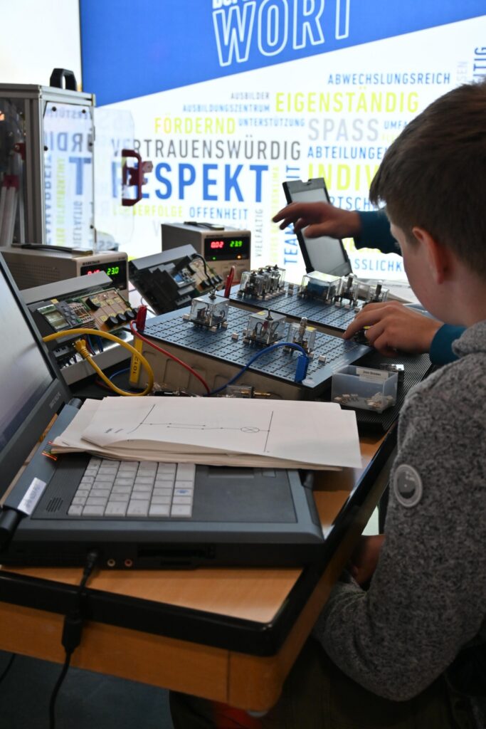 Schüler arbeitet an einem Tisch mit technischen Geräten und einem Laptop.