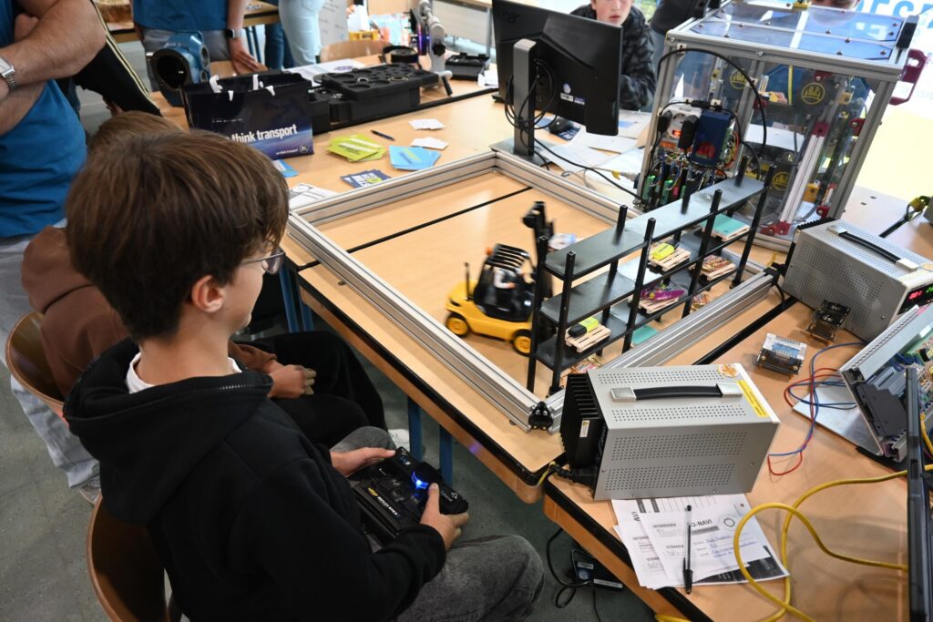 Schüler steuert ein Modellauto auf einer Tischplattform mit technischen Geräten.