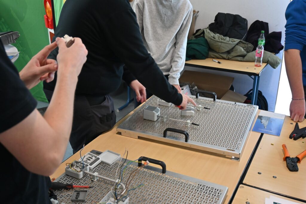 Schüler arbeiten an technischen Projekten an Tisch mit Werkzeugen und Materialien.