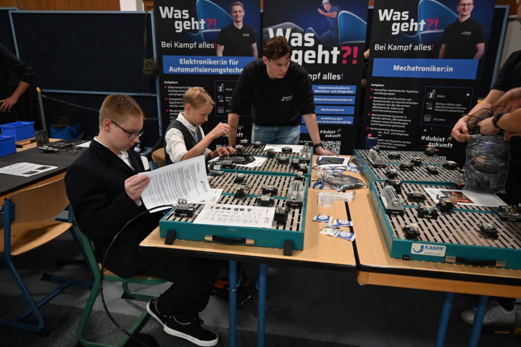 Schüler arbeiten an Technikprojekten an einem Stand mit Informationsmaterial.